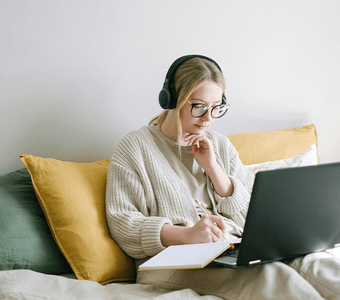 A woman sitting on the couch with headphones on and looking at her laptop.